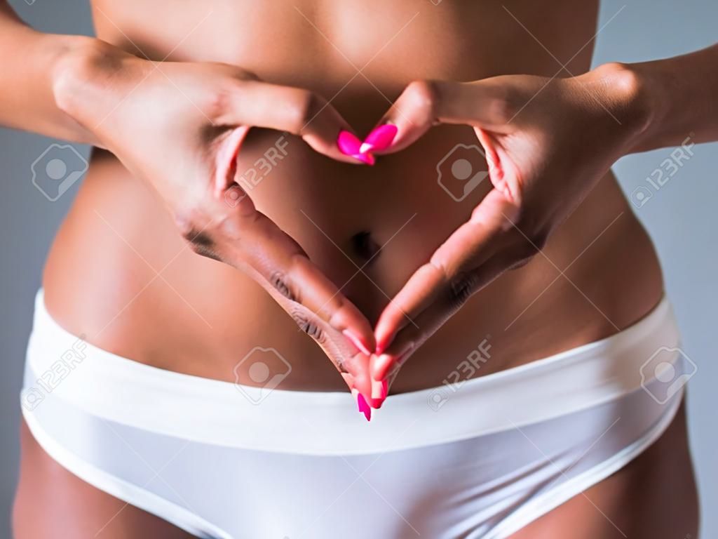 Cropped image of beautiful Afro American girl showing heart on her stomach, on gray background