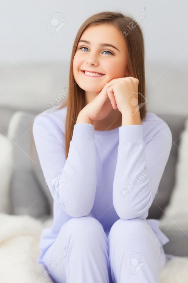 Attraktive Jugendlichen im Pyjama schaut weg und lächelt beim Sitzen auf Couch zu Hause