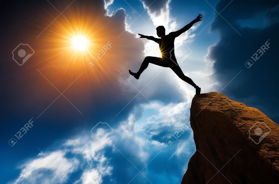 silhouette d'un homme sautant d'une falaise dans la direction du soleil lumineux