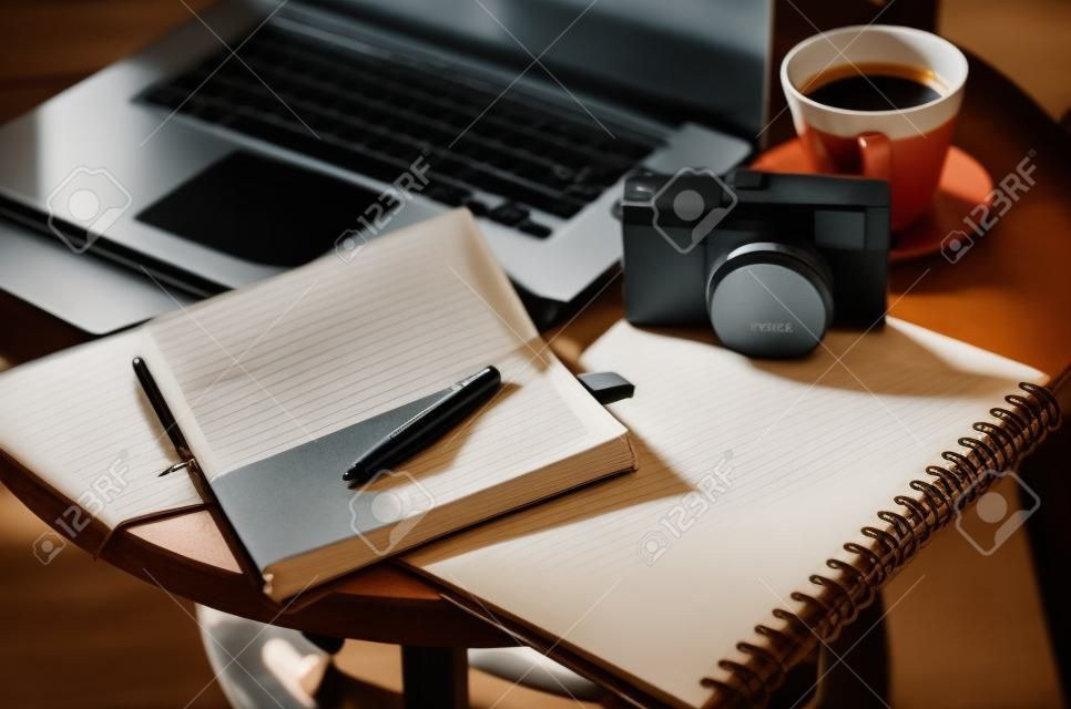 Laptop and pen on notebook beside camera,coffee cup upstairs table vintage style