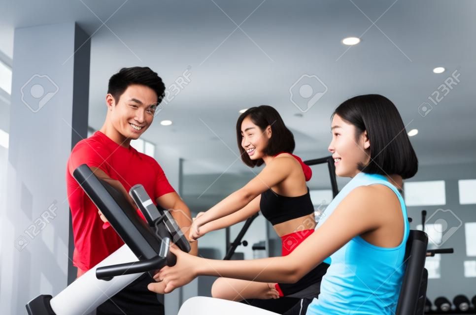 asian young woman slim body exercising on bicycle machine with young man personal trainer in fitness gym, bodybuilder, healthy lifestyle, fitness, workout and sport training concept, soft focus