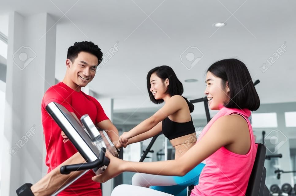 asian young woman slim body exercising on bicycle machine with young man personal trainer in fitness gym, bodybuilder, healthy lifestyle, fitness, workout and sport training concept, soft focus