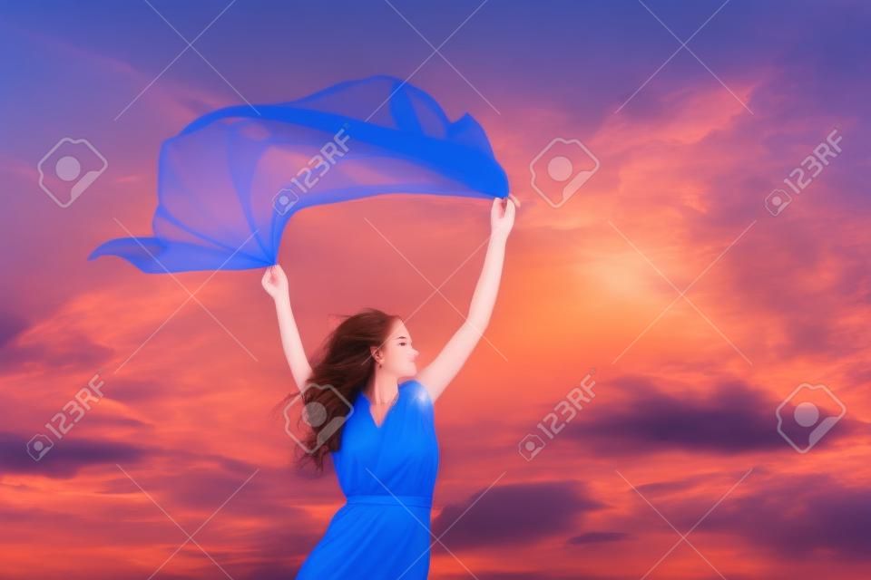 Mooie jonge vrouw op zonsondergang achtergrond met blauw weefsel.