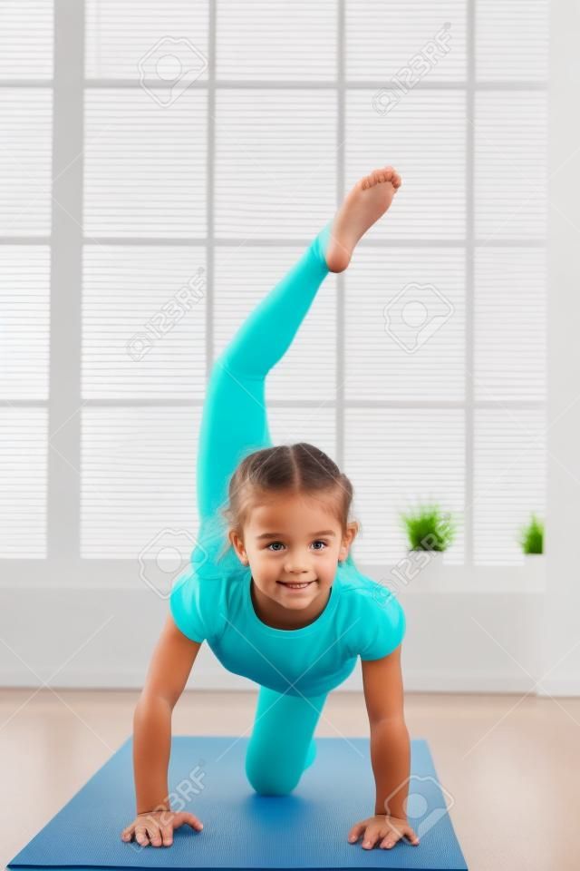 Little girl doing yoga exercise in fitness studio with big windows on background