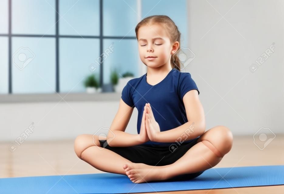 小女孩坐在封閉的眼睛和雙手蓮花位置在健身室與背景的大窗戶