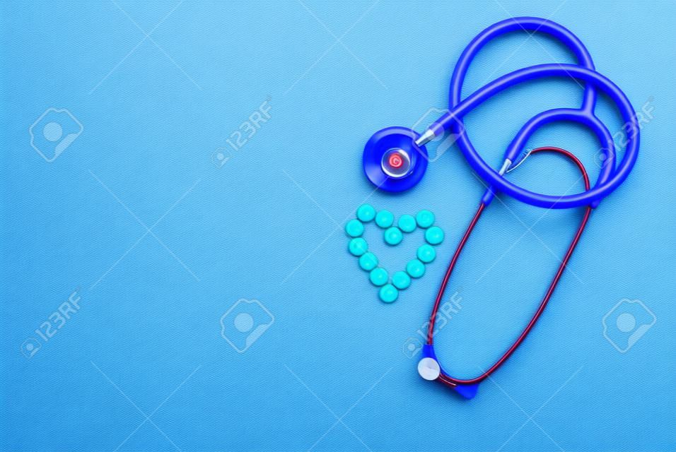 Red stethoscope with tablets, pills on blue background.