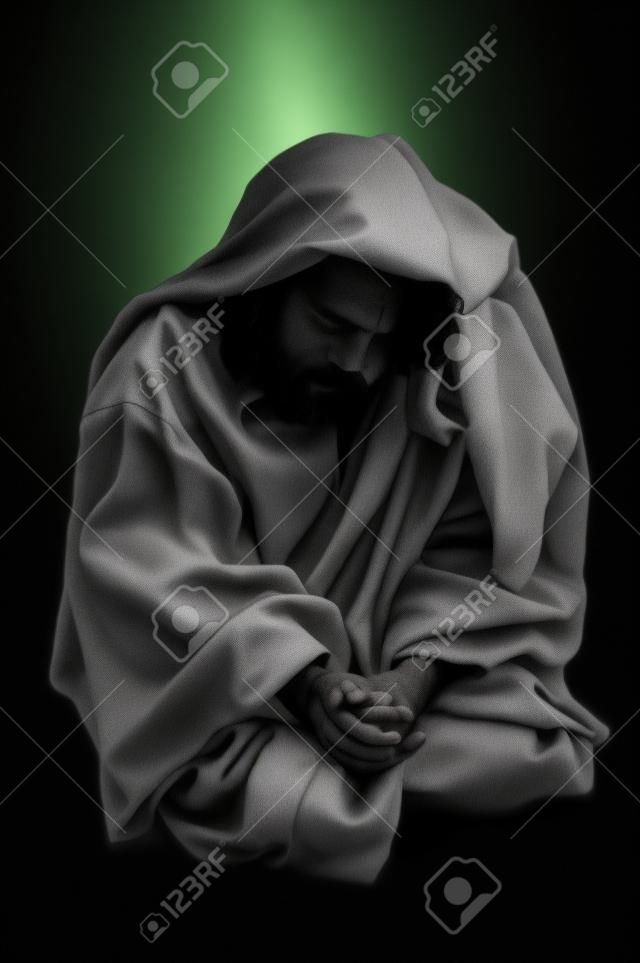 Jesús orando de rodillas sobre un fondo negro