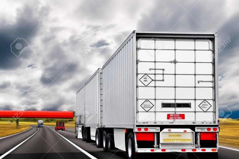 Three trailer road train transporting commercial cargo in USA highway. White long heavy vehicle rear, travels with cloudy sky background.