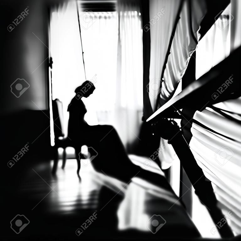 Zwart-wit portret van een bruid aan het raam. Een prachtig silhouet van een vrouw