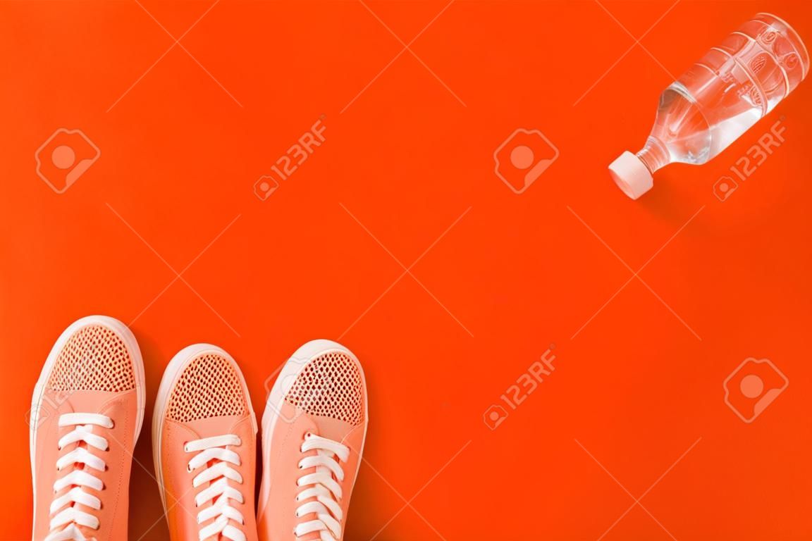 Light orange sneakers and a bottle of water on a orange background with a place for an inscription.