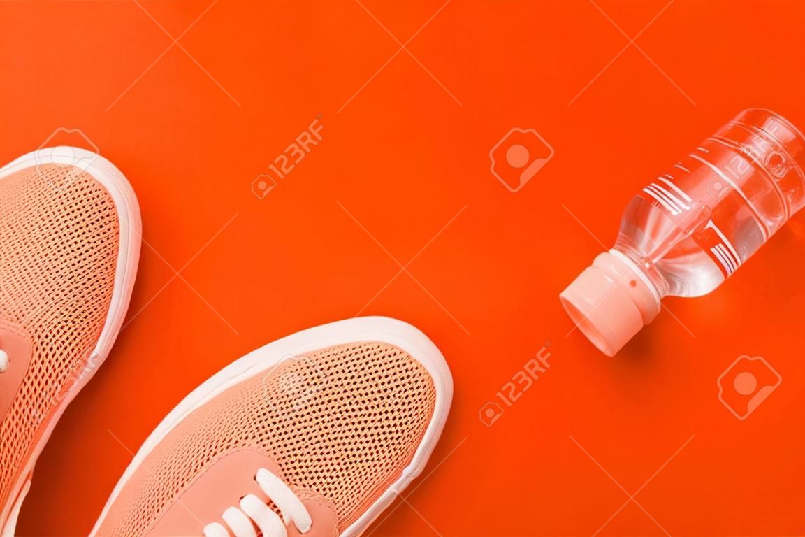 Licht oranje sneakers en een fles water op een oranje achtergrond met een plaats voor een inscriptie.