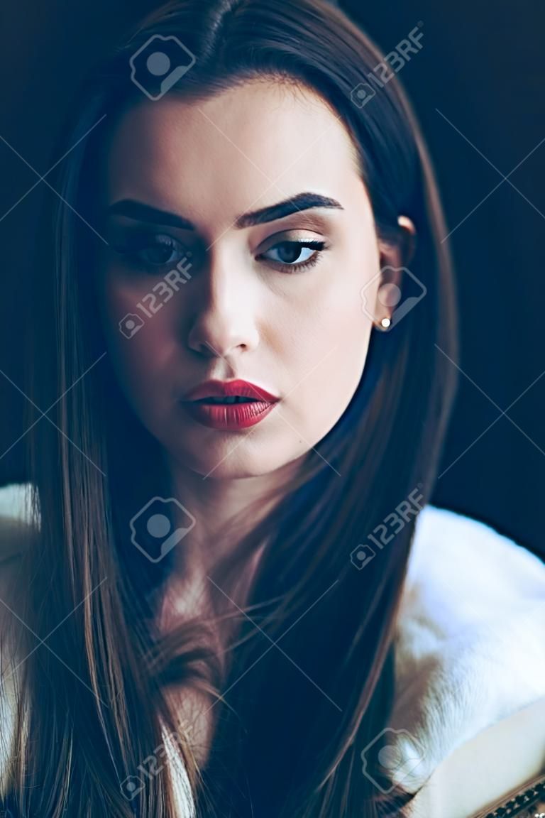 Young beautiful woman portrait, close-up. Pretty girl with red lipstick and stylish hairdo. Pensive look of the female model
