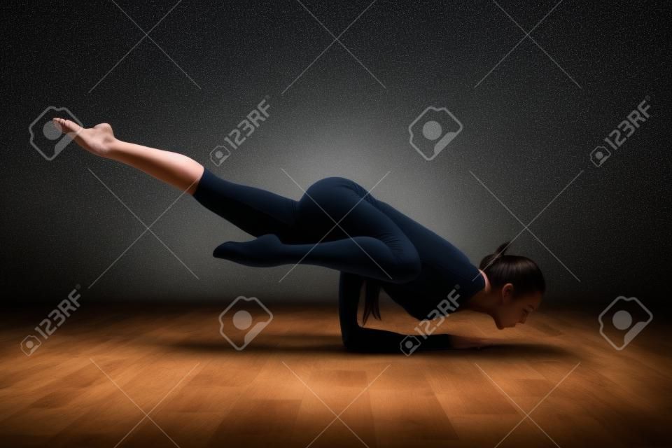 Młoda kobieta ćwiczy jogę w pozie płotkowej w ciemnym pokoju