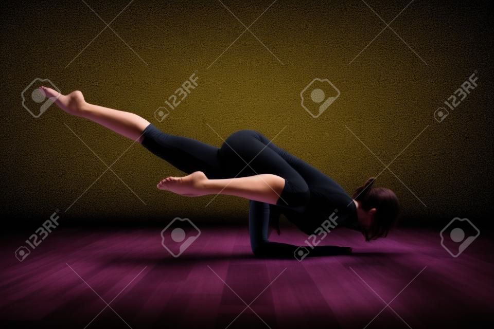 Mujer joven practicando yoga haciendo pose de vallista en cuarto oscuro