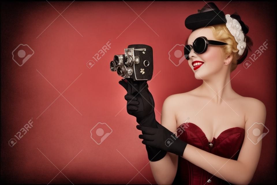 A fotó a pin-up girl in fűzőt és kesztyűt gazdaság vintage 8mm kamera.