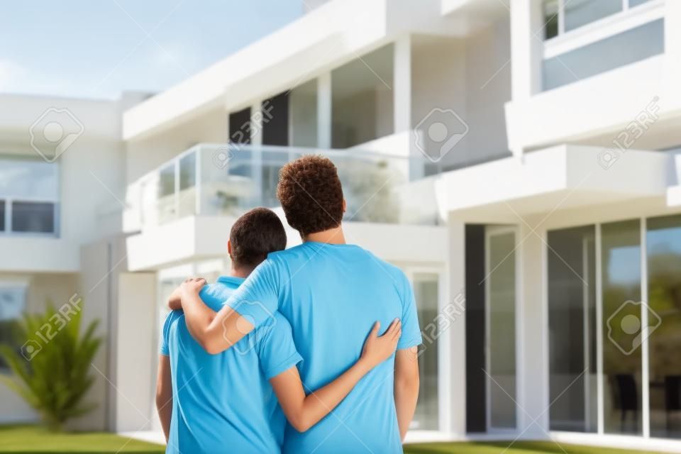 la pareja se abraza en frente de la nueva casa grande moderno, de visión trasera al aire libre espalda mirando a casa de sus sueños