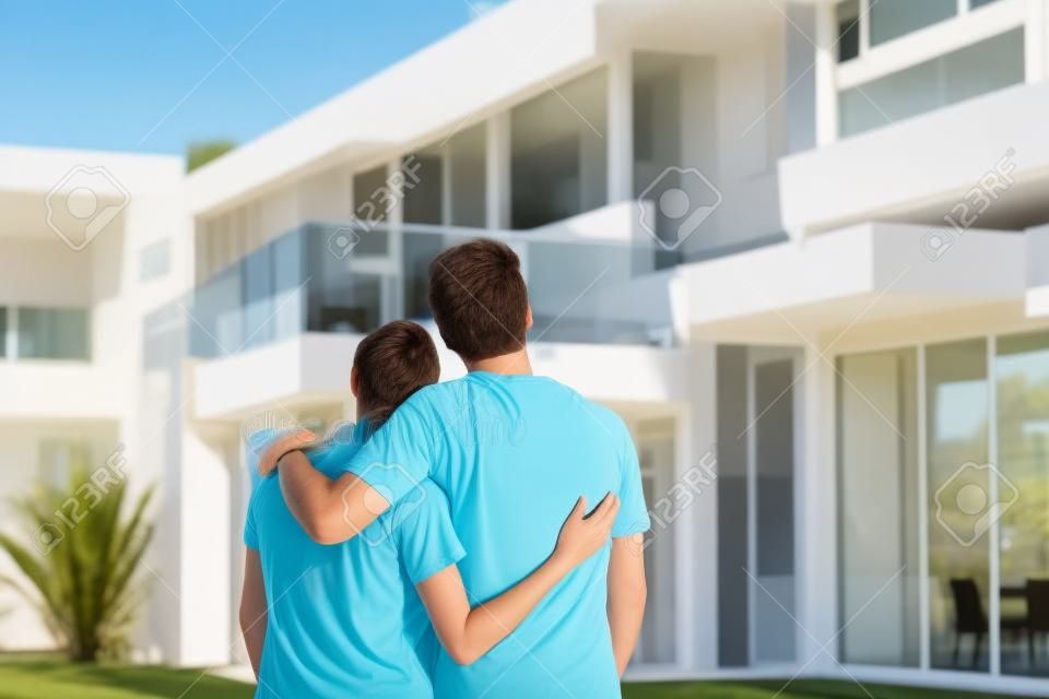 夫婦擁抱在新的現代大房子前，戶外後視圖回望著自己的夢想家園