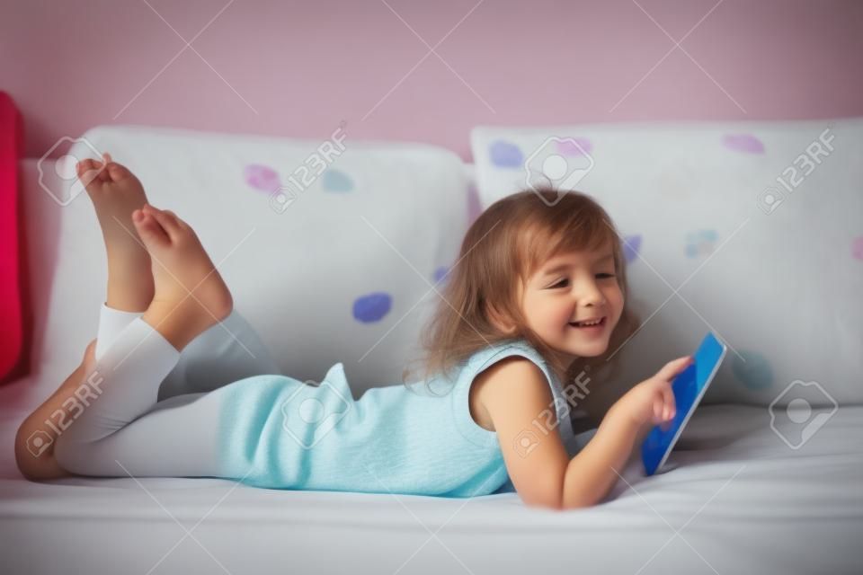 heureuse petite fille couchée sur le lit avec la tablette
