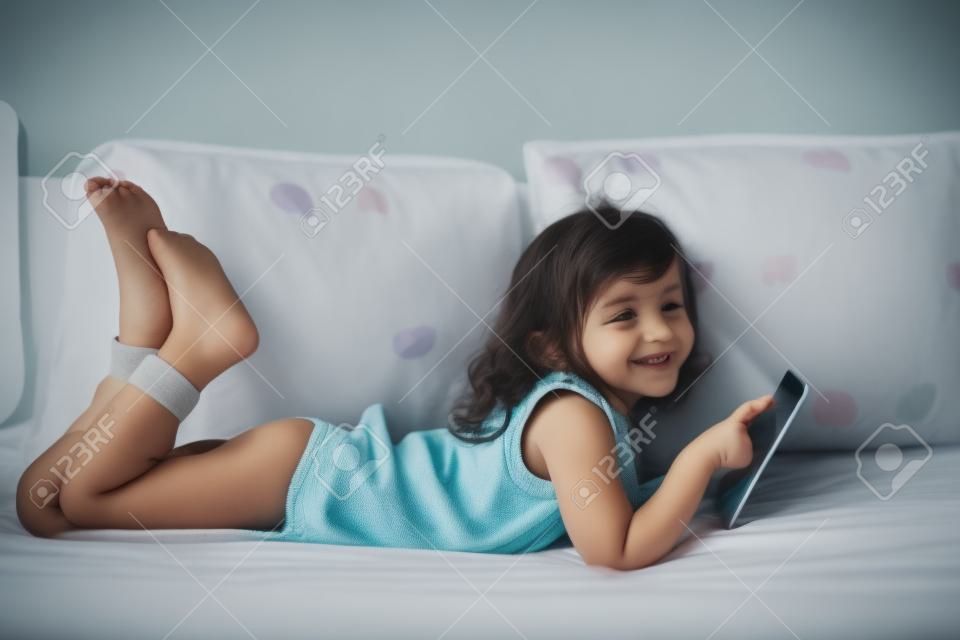 heureuse petite fille couchée sur le lit avec la tablette