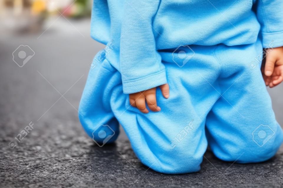 Um garoto mijando em suas calças na rua - conceito de molhar a cama. Criança mija nas roupas.