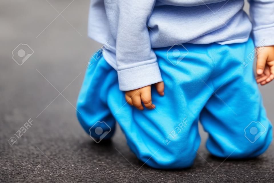 Um garoto mijando em suas calças na rua - conceito de molhar a cama. Criança mija nas roupas.