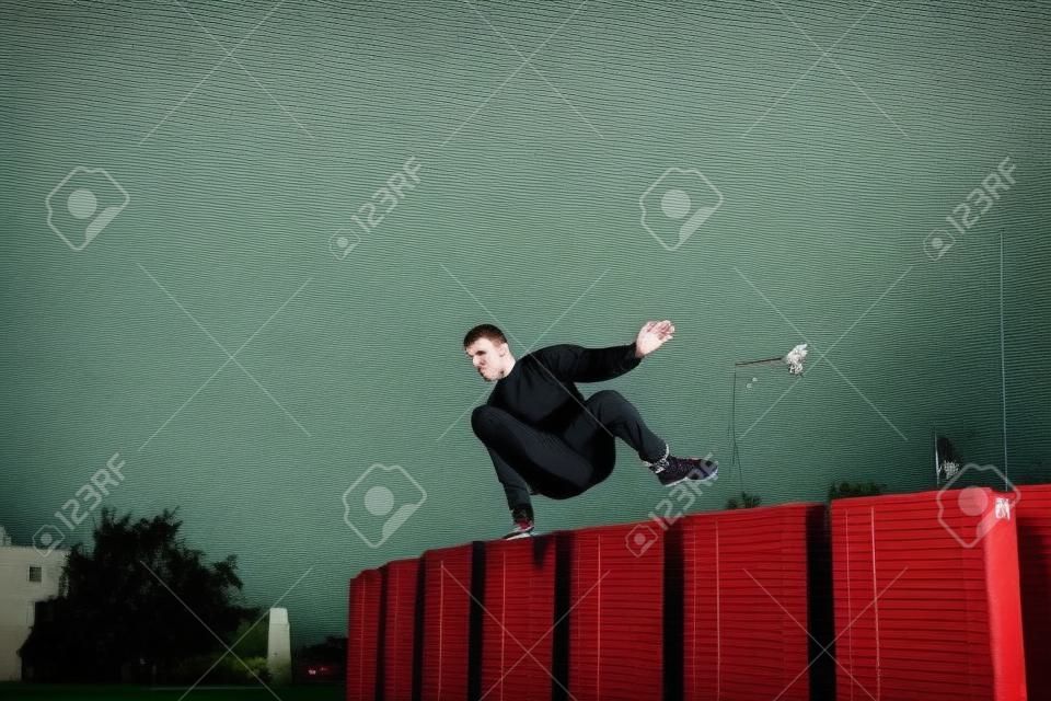 Un homme de race blanche s'entraîne au parkour en sautant par-dessus un haut.