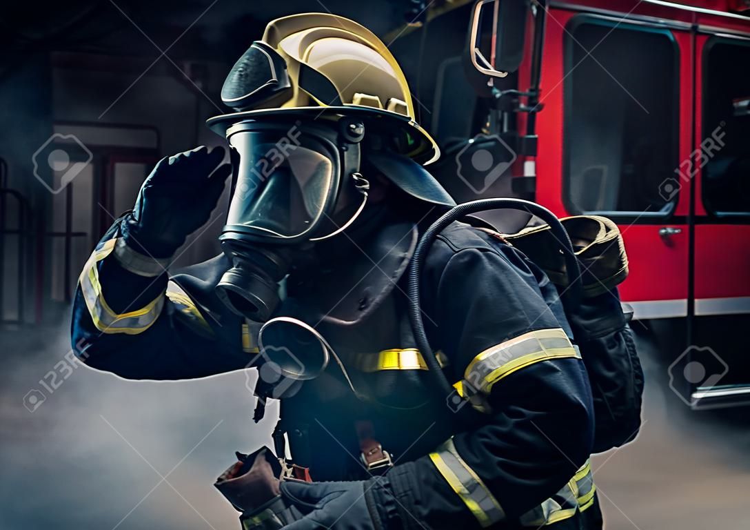 Portret strażaka ubranego w rozjazdy strażackie i hełm na ciemnym tle z dymem i niebieskim światłem