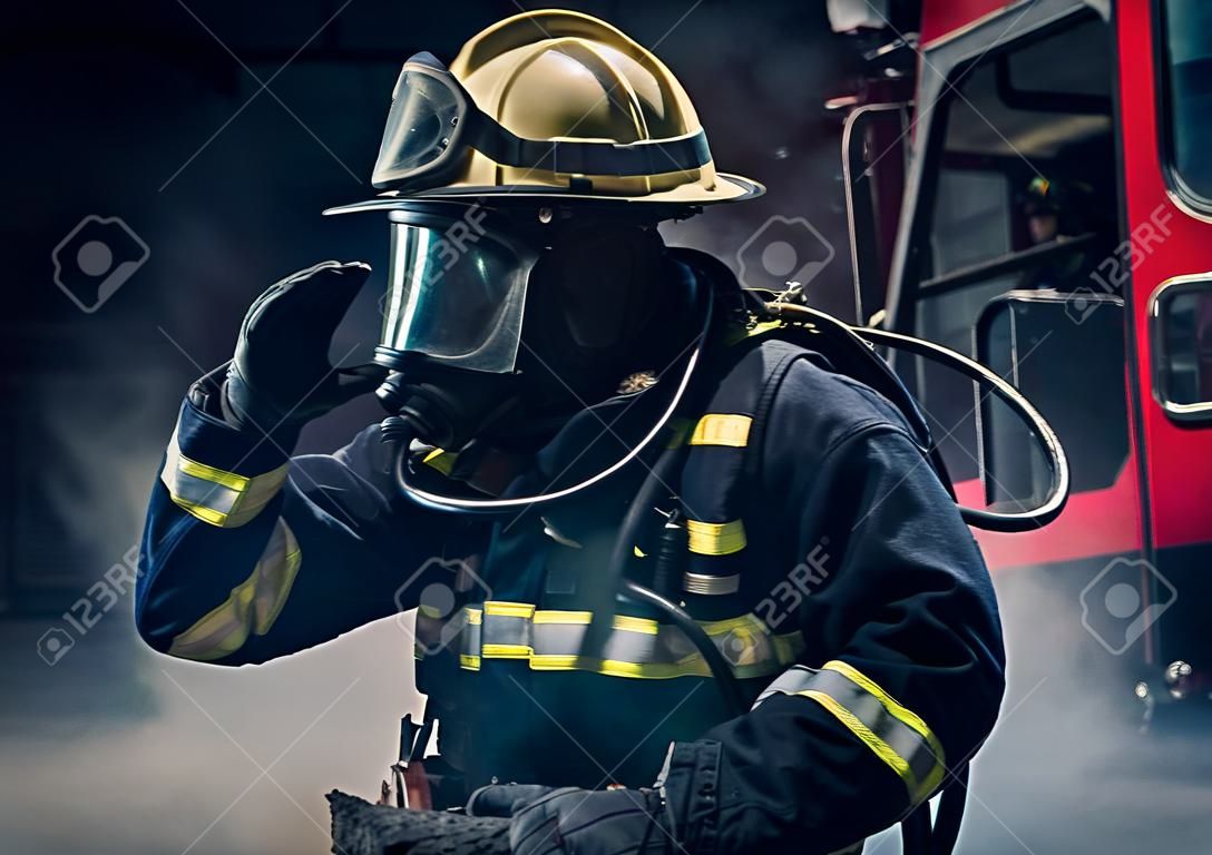 Portret strażaka ubranego w rozjazdy strażackie i hełm na ciemnym tle z dymem i niebieskim światłem