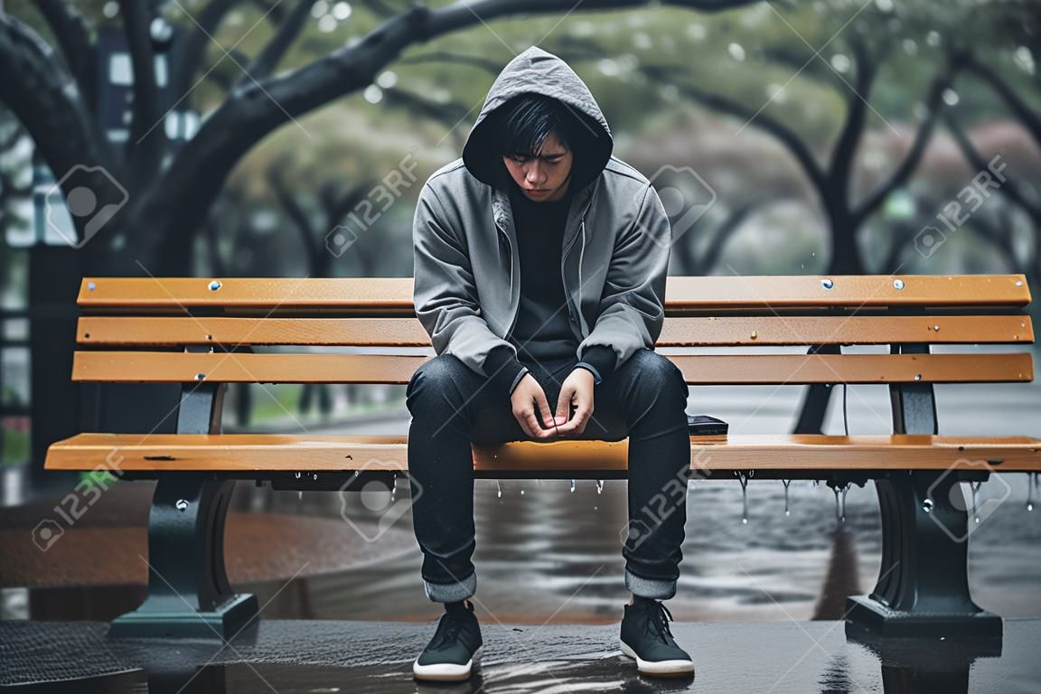 young handsome asian hipster man sitting on bench in the rain