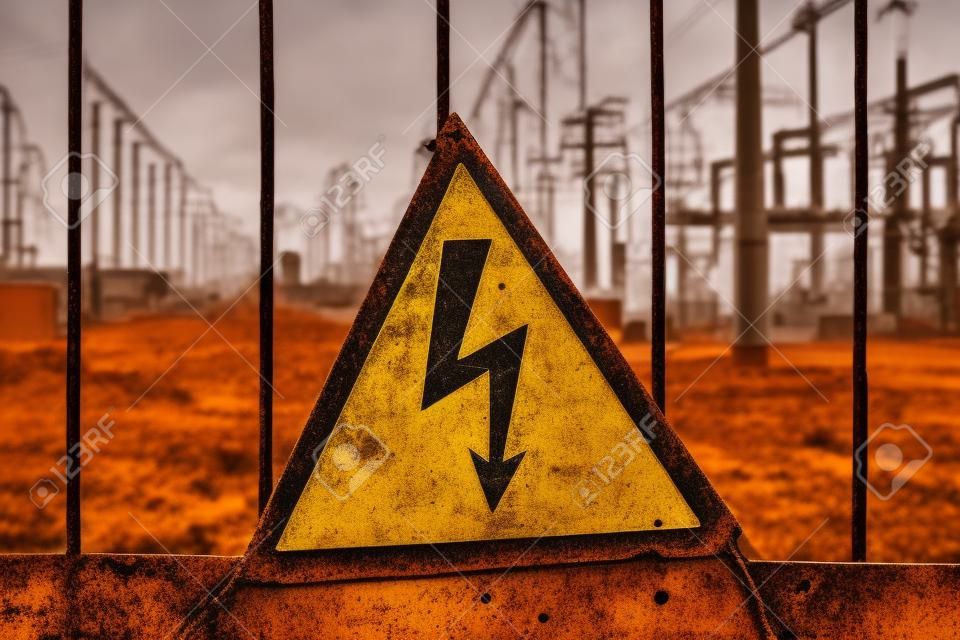 고전압 경고 표시가 있는 근접 오래된 세 녹슨 삼각형 금속판. 변압기와 배전선이 있는 발전소. 입장 금지.