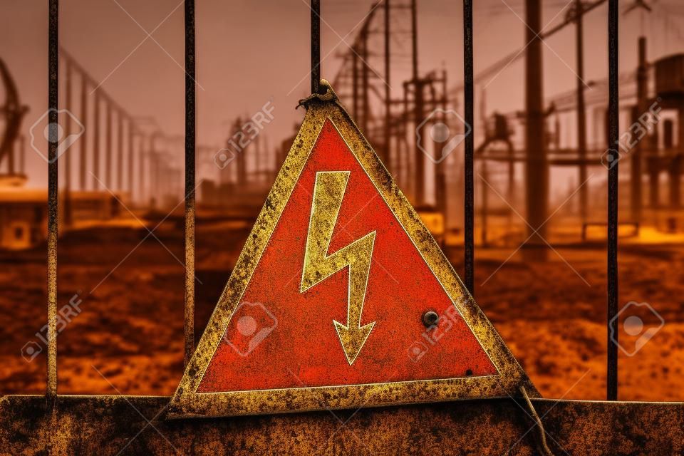 Close-up old aged rusty triangle metal plate with High voltage warning sign. Power station with transformers and electricity distribution lines. Keep out.