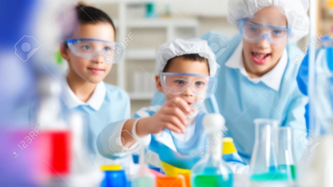 Elementary School Science Classroom: Enthusiastic Teacher Explains Chemistry to Diverse Group of Children, Little Boy Mixes Chemicals in Beakers. Children Learn with Interest