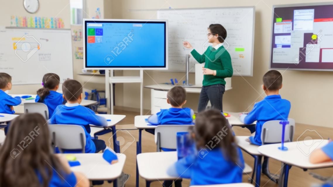Le professeur de sciences de l'école élémentaire utilise un tableau blanc numérique interactif pour montrer à une salle de classe pleine d'enfants comment la programmation logicielle fonctionne pour la robotique. Classe de sciences, enfants curieux écoutant attentivement