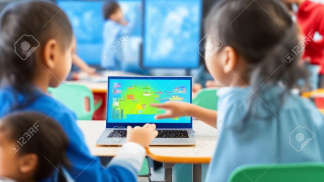 Elementary School Science Class: Sobre o Ombro Little Boy e Girl Use Laptop com tela mostrando software de programação. Professor de física explica lição para uma classe diversificada cheia de crianças inteligentes