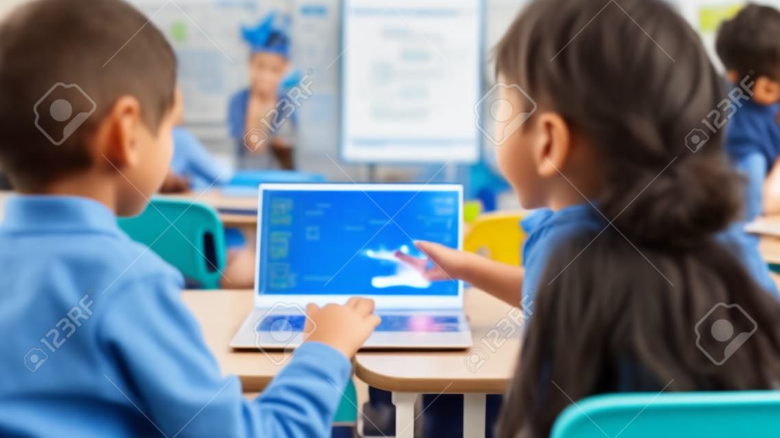 Elementary School Science Class: Sobre o Ombro Little Boy e Girl Use Laptop com tela mostrando software de programação. Professor de física explica lição para uma classe diversificada cheia de crianças inteligentes