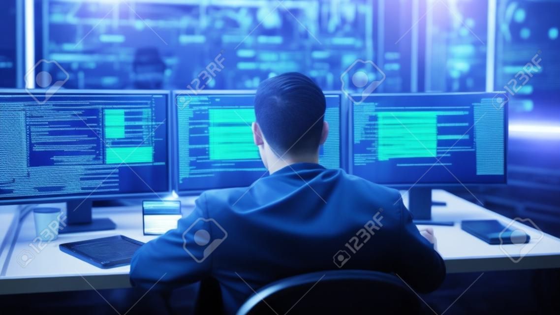 IT-Spezialist arbeitet an einem Personal Computer mit Bildschirmen, auf denen Softwareprogramme mit Codierungssprachenschnittstelle angezeigt werden. Im Hintergrundtechnikraum des Rechenzentrums mit professionellem Arbeiten