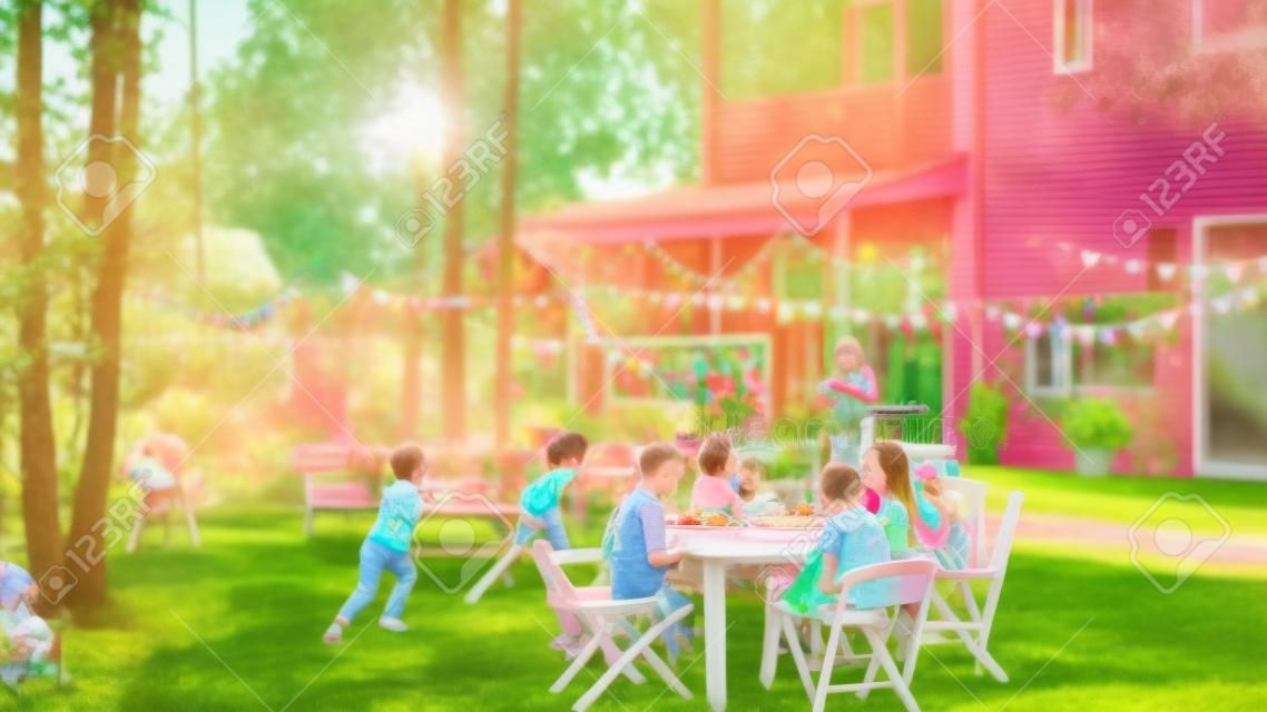 Wielkie rodzinne przyjęcie w ogrodzie, zebrane przy stole rodzina, przyjaciele i dzieci. ludzie piją, podają naczynia, żartują i dobrze się bawią. dzieci biegają wokół stołu.