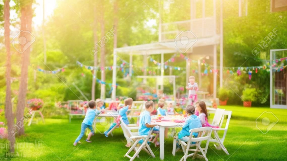 Celebrazione della festa in giardino in grande famiglia, riuniti a tavola Famiglia, amici e bambini. Le persone bevono, passano i piatti, scherzano e si divertono. I bambini corrono intorno al tavolo.