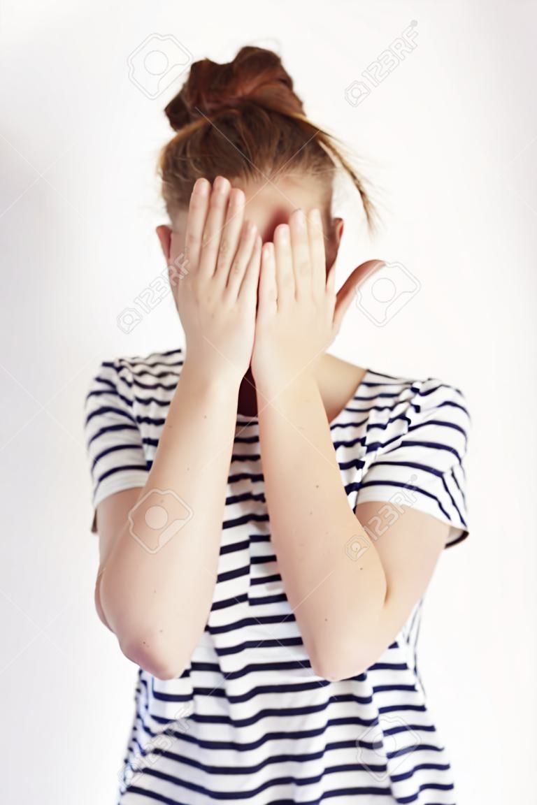 Retrato da mulher tímida que cobre o rosto com as mãos no tiro do estúdio