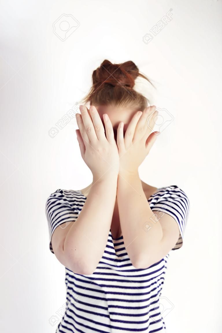 Retrato da mulher tímida que cobre o rosto com as mãos no tiro do estúdio