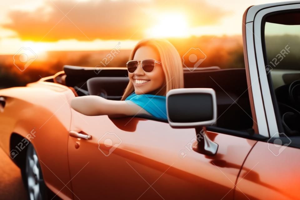 Piękna kobieta siedzi w samochodzie o zachodzie słońca
