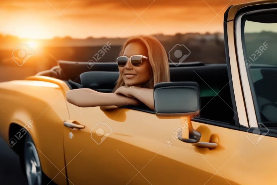 Mooie vrouw zitten in de auto bij zonsondergang