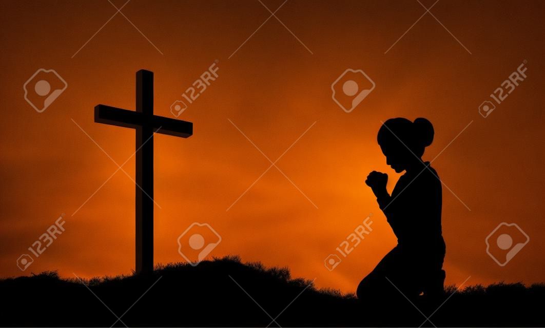 Silhouette of a woman praying under the cross