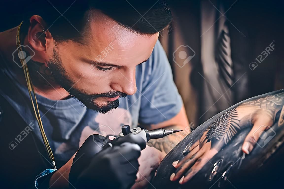 Professional tattoo artist makes a tattoo on a young man's hand
