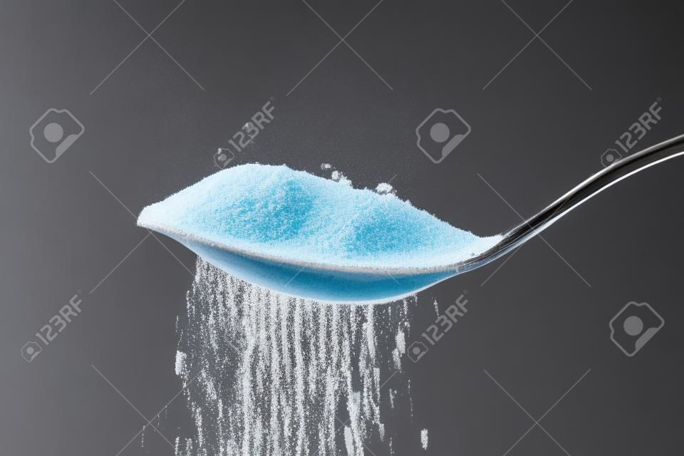 zucchero semolato versando da un cucchiaino su sfondo nero