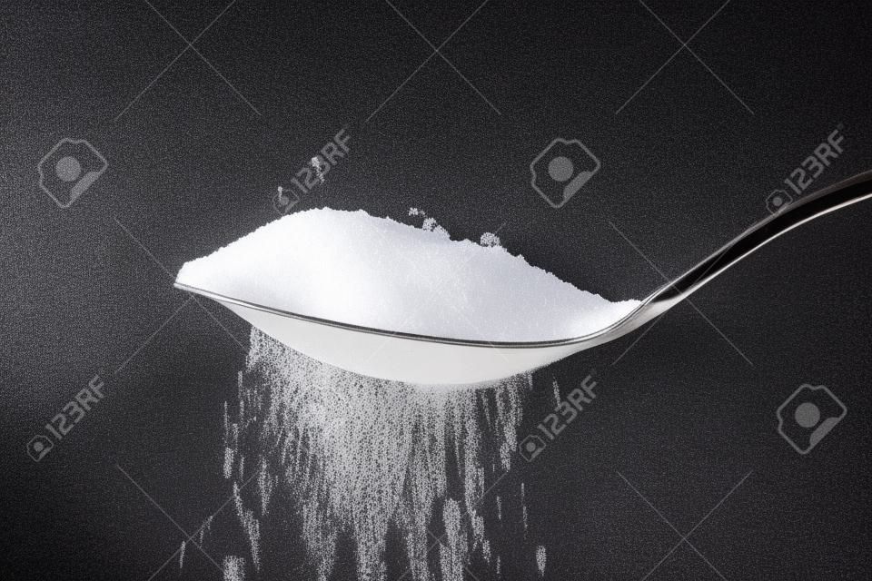 zucchero semolato versando da un cucchiaino su sfondo nero
