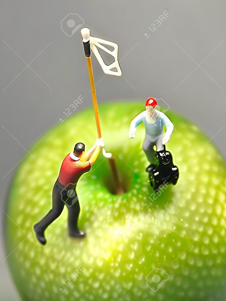 Minigolf auf Apfel Makro-Aufnahme von Golf-Figuren spielen Runde oben auf grünem Apfel