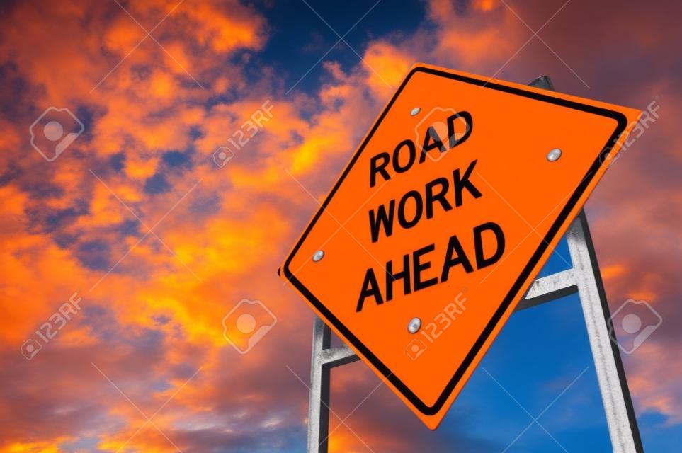 Image of a bright orange road work ahead sign against a blue sky with light clouds