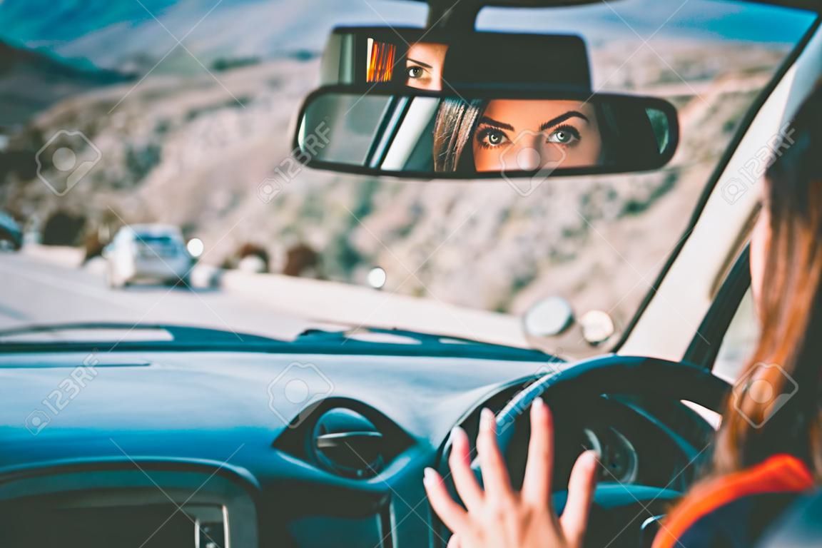 The eyes of a beautiful young woman seen through a back view mirror of her car as she enjoys driving.  Toned picture