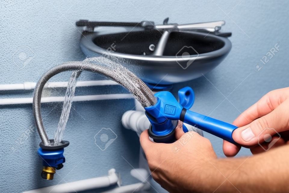 El fontanero fija la manguera de conexión trenzada al grifo de agua antes de instalar el grifo en el lavabo del baño.